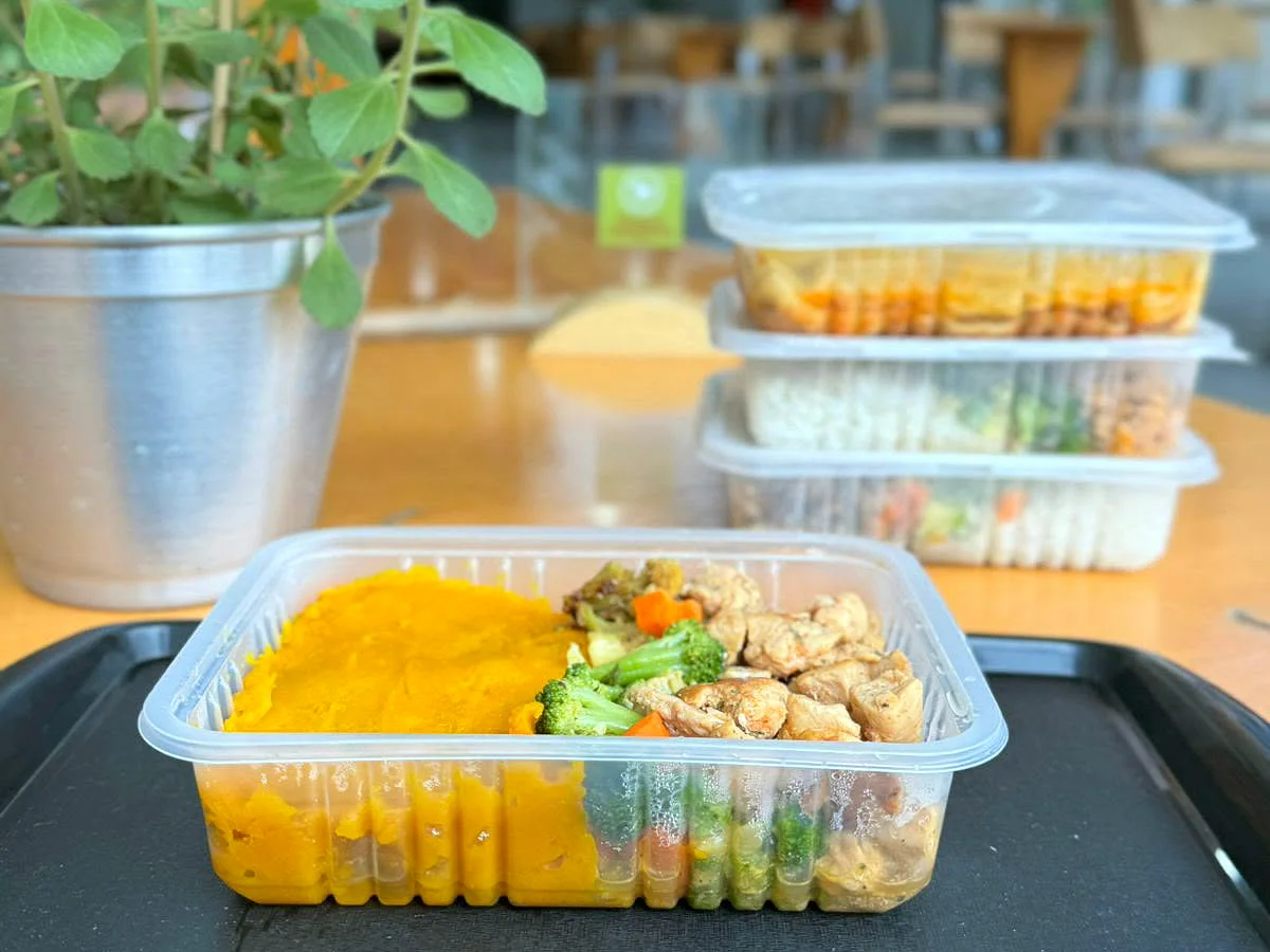 Marmita Fresco Tempero com purê de moranga, frango e legumes, e marmitas congeladas empilhadas ao fundo